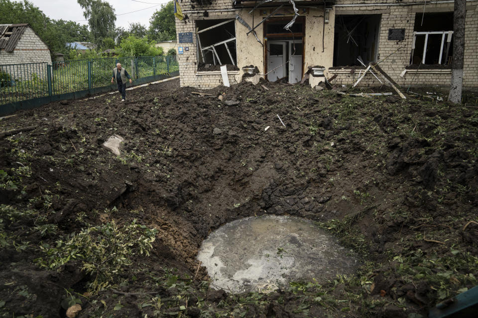 A local man walks in front of a crater and damaged school after Russian shelling at residential area in Chuhuiv, Kharkiv region, Ukraine, Saturday, July 16, 2022. (AP Photo/Evgeniy Maloletka)