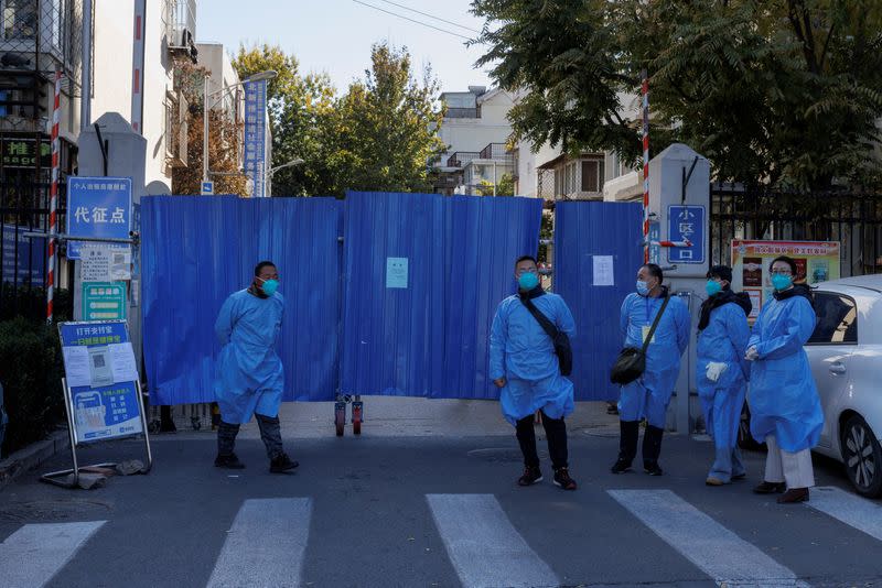 Officials wearing protective aprons stand outside the boarded-up gate of a residential compound that was placed under lockdown as outbreaks of coronavirus disease (COVID-19) continue in Beijing