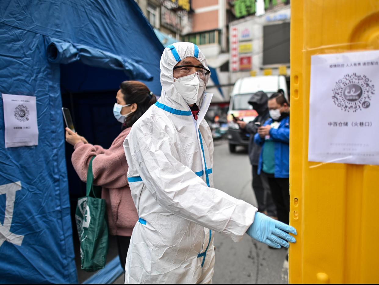 <p>A man wearing a protective suit controls the access to a market in Wuhan in March 2020</p> (AFP via Getty Images)