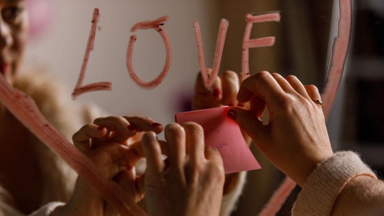 woman applying a sticky note with the words ''miss you'' on the mirror