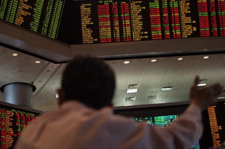A man sits below a digital stocks display at Malaysia Stock Exchange in Kuala Lumpur, December 12, 2014