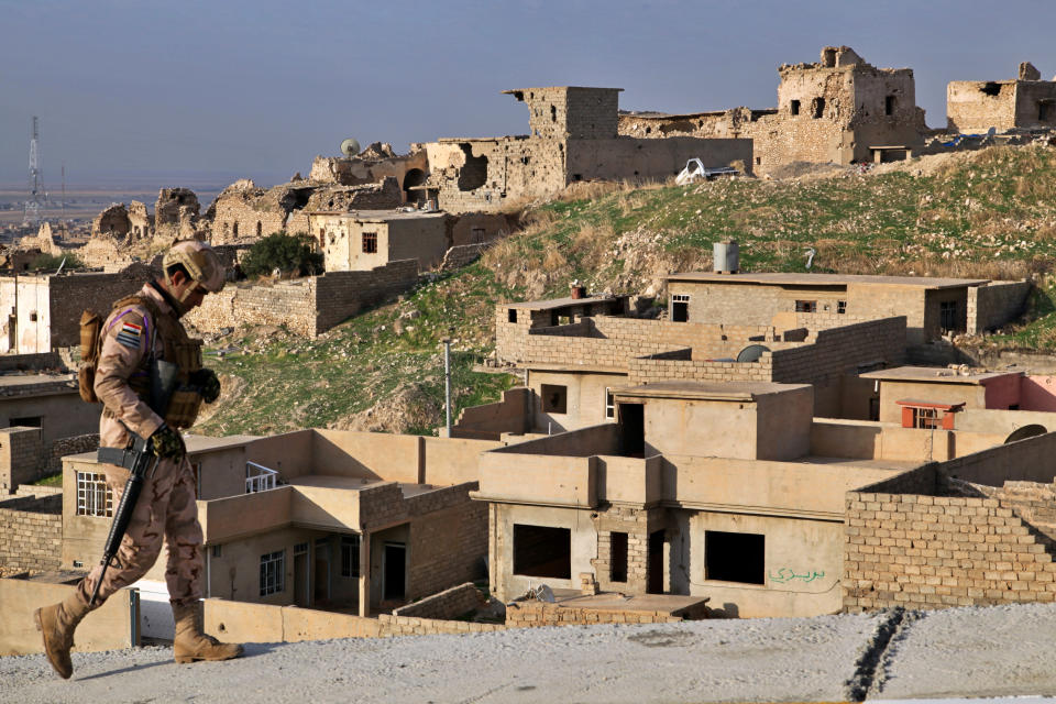 An Iraqi army soldier walks by ruins still deserted three years since the defeat of the Islamic State group in Sinjar, Iraq. Friday. Dec. 4, 2020. A new agreement aims to bring order to Iraq's northern region of Sinjar, home to the Yazidi religious minority brutalized by the Islamic State group. Since IS's fall, a tangled web of militia forces have run the area, near the Syrian border. Now their flags are coming down, and the Iraqi military has deployed in Sinjar for the first time in nearly 20 years. (AP Photo/Samya Kullab)