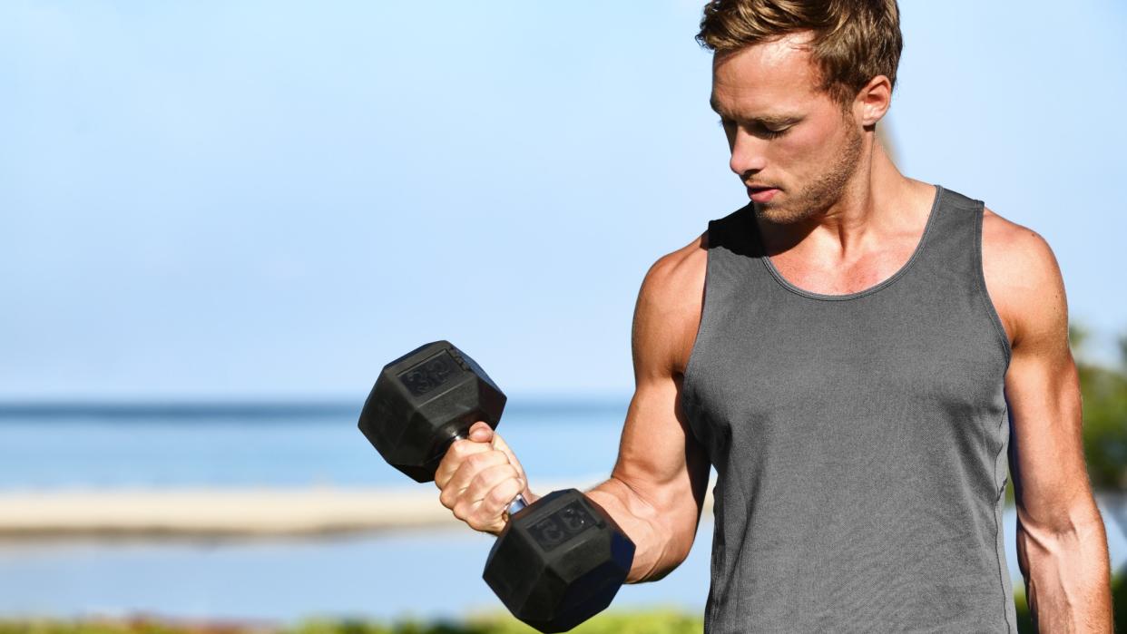  Man holding a dumbbell in right hand with elbow flexed during arm workout outdoors. 