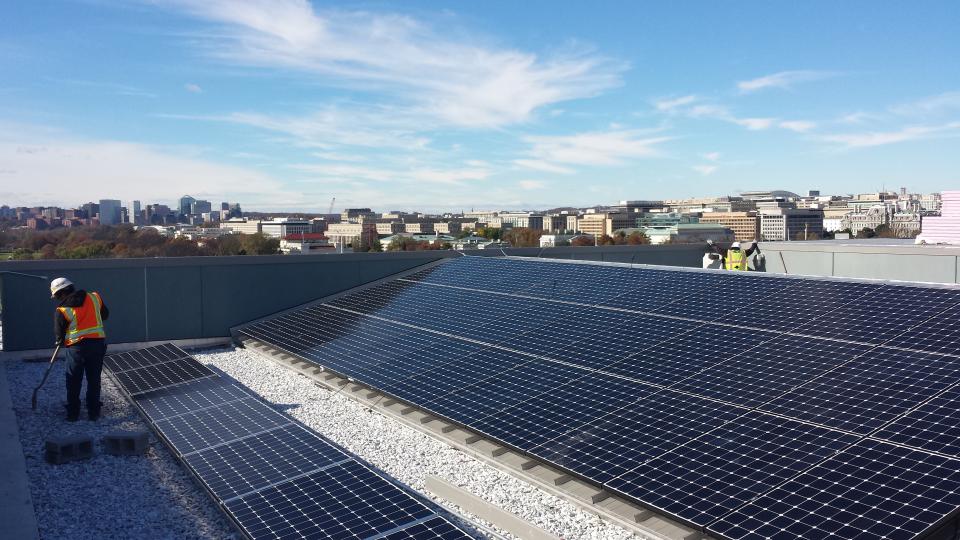 Rows of solar panels on a roof, with view of skyline behind.