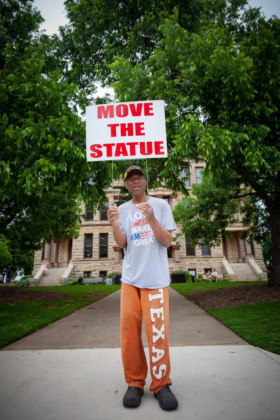 A man holds a sign that says "Move the Statue" as he stands in front of a courthouse.