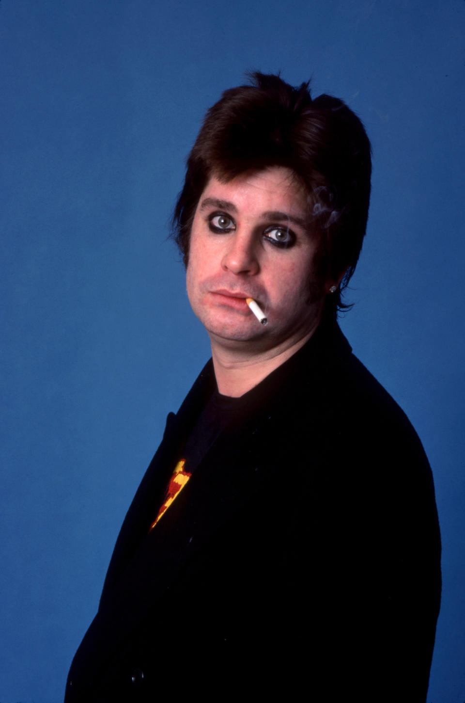 Ozzy with short hair and eye makeup and smoking a cigarette