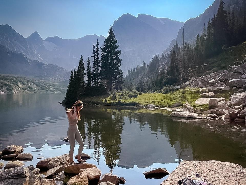 Emily walks across rocks in a lake that's surrounded by mountains and trees.