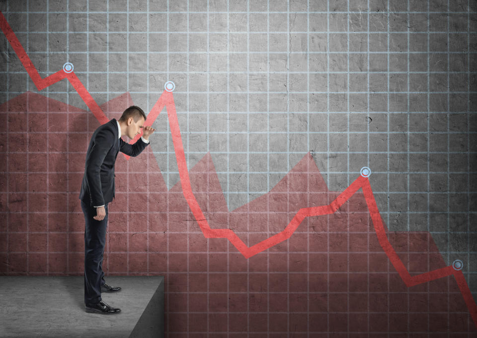 A businessman looking at a line chart plunging downward