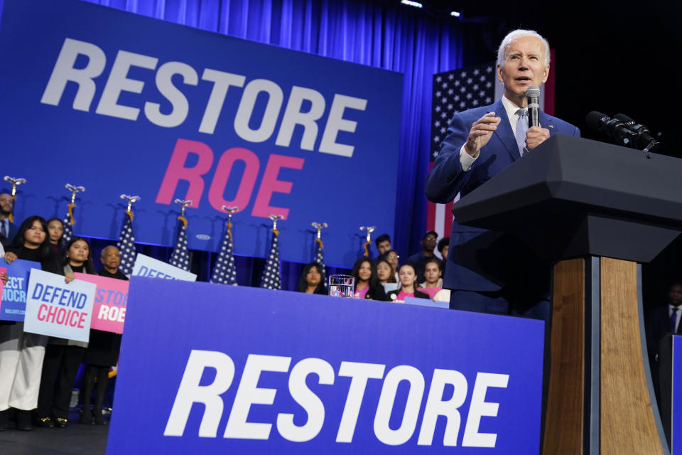 President Biden speaks, surrounded by blue posters saying: Restore Roe.