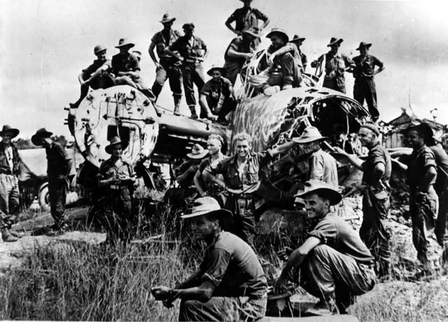 Members of the battalion from the Australian 9th Division climb over a wrecked Japanese bomber abandoned on the edge of the strip in Borneo