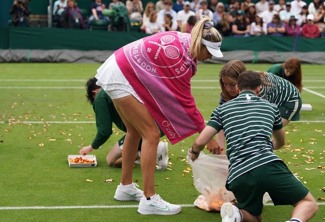 Katie Boulter helps ground staff clear confetti from Court 18 after a Just Stop Oil protest 