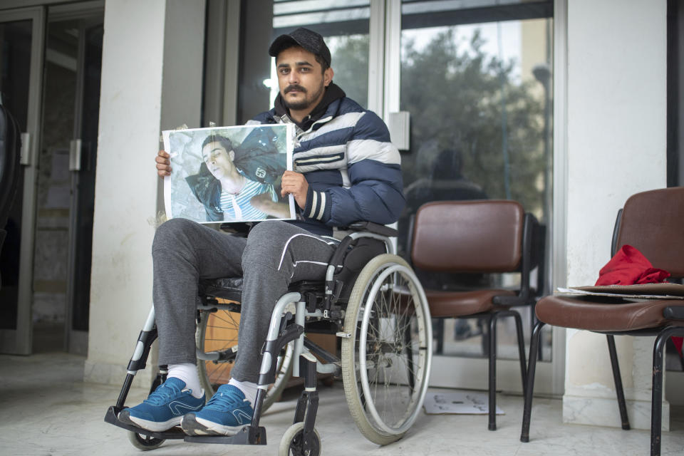 Rached El Arbi, 30, a protester who was paralyzed after being shot during Tunisia's democratic uprising 10 years ago, poses for a portrait while holding an image of himself, in Tunis, Tunisia, Tuesday, Jan. 12, 2021. El Arbi, now 30, has been paralyzed since being shot while protesting the autocratic regime of Tunisia's President Zine El Abidine Ben Ali, who was overthrown on Jan. 14, 2011. A photo of El Arbi hospitalized at the time went viral across the Arab world. (AP Photo/Mosa'ab Elshamy)