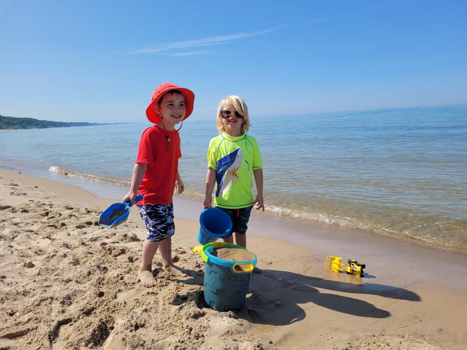 Two children playing on a beach, with sand buckets and toys.