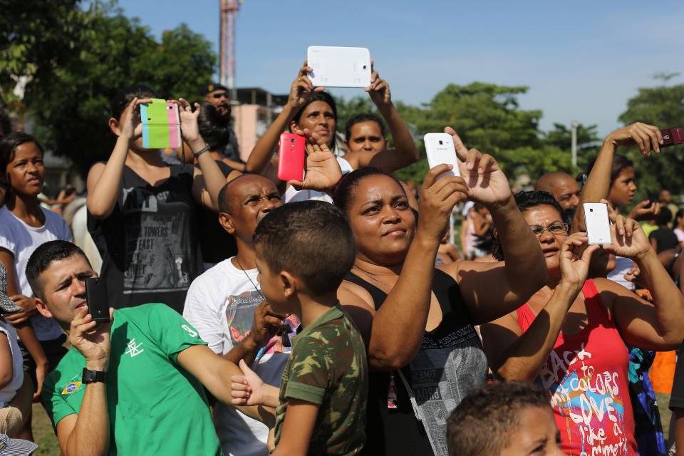 Residents of Vila Pinheiro slum take photos with their as they watch the flag raising ceremony during a police operation to occupy the Mare slum complex in Rio de Janeiro, Brazil, Sunday, March 30, 2014.ce The Mare complex of slums, home to about 130,000 people and located near the international airport, is the latest area targeted for the government's "pacification" program, which sees officers move in, push out drug gangs and set up permanent police posts. (AP Photo/Leo Correa)