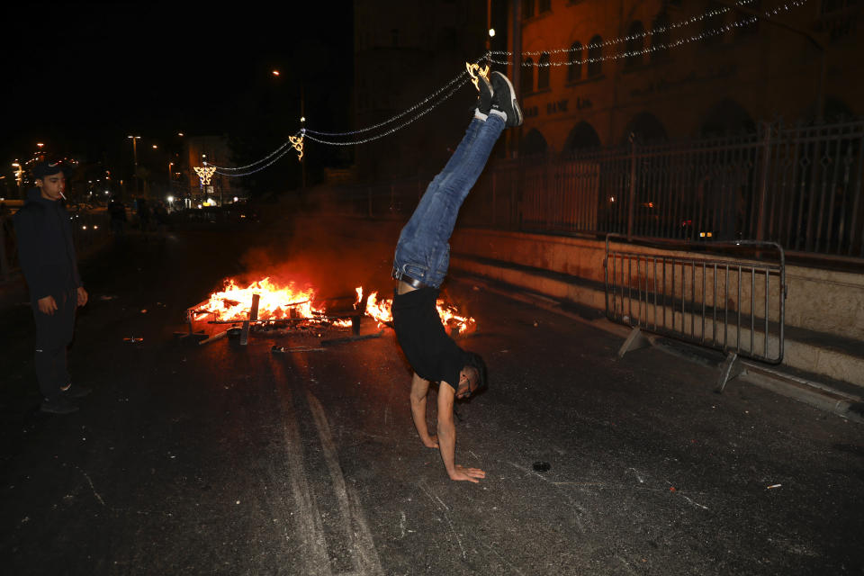 A Palestinian protester does a handstand next to a fire which was set on a road during clashes with Israeli police near Damascus Gate just outside Jerusalem's Old City, Sunday, May 9, 2021. Israeli police have been clashing with Palestinian protesters almost nightly in the holy city's worst religious unrest in several years. (AP Photo/Ariel Schalit)