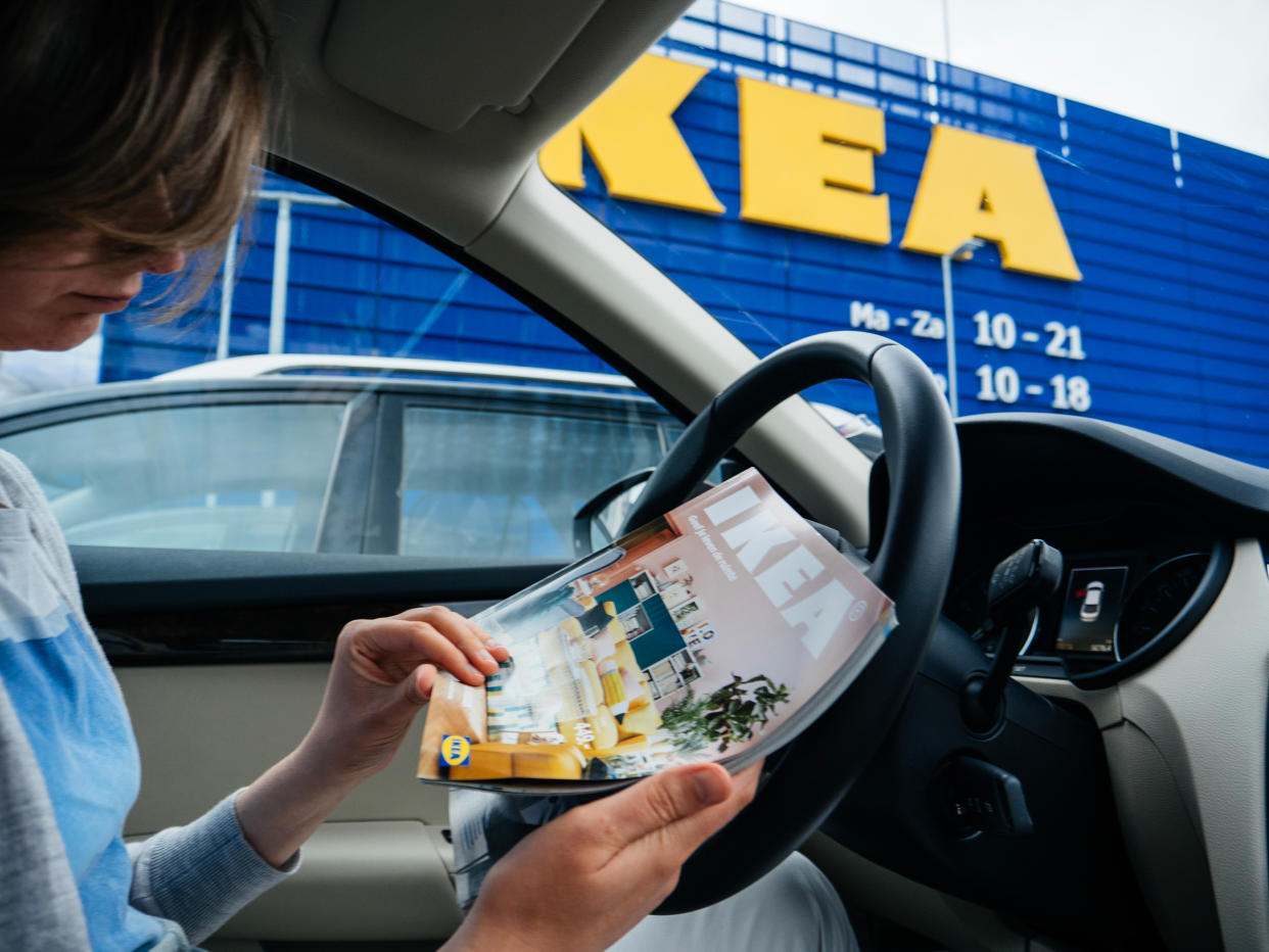 Delft: Elegant woman reading IKEA furniture magazine catalog inside car parked on the wide IKEA parking in the main store in netherlands, headquarter of IKEA Global