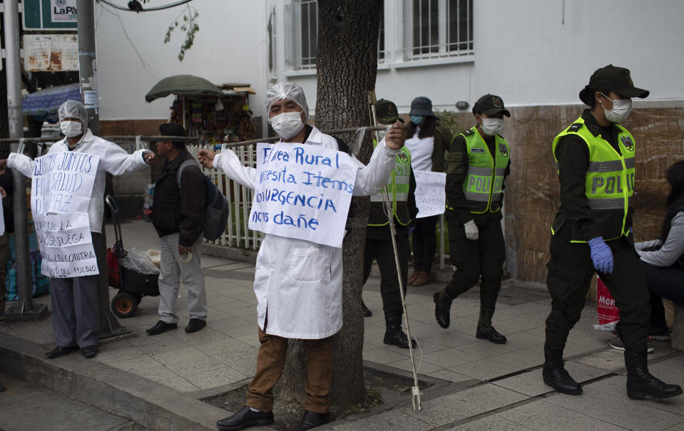 FILE - In this March 18, 2020 file photo, doctors protest for more physicians and better working conditions, to deal the new coronavirus, outside the Health Ministry in La Paz, Bolivia. The sign at center reads in Spanish: "Rural areas urgently need more personnel. Don't hurt us." (AP Photo/Juan Karita, File)