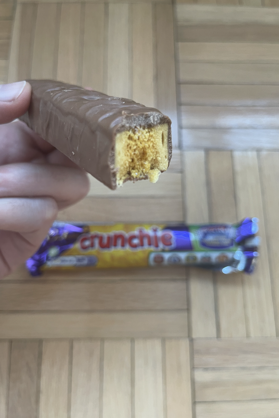A person holding a bitten Crunchie chocolate bar with another unopened one in the background