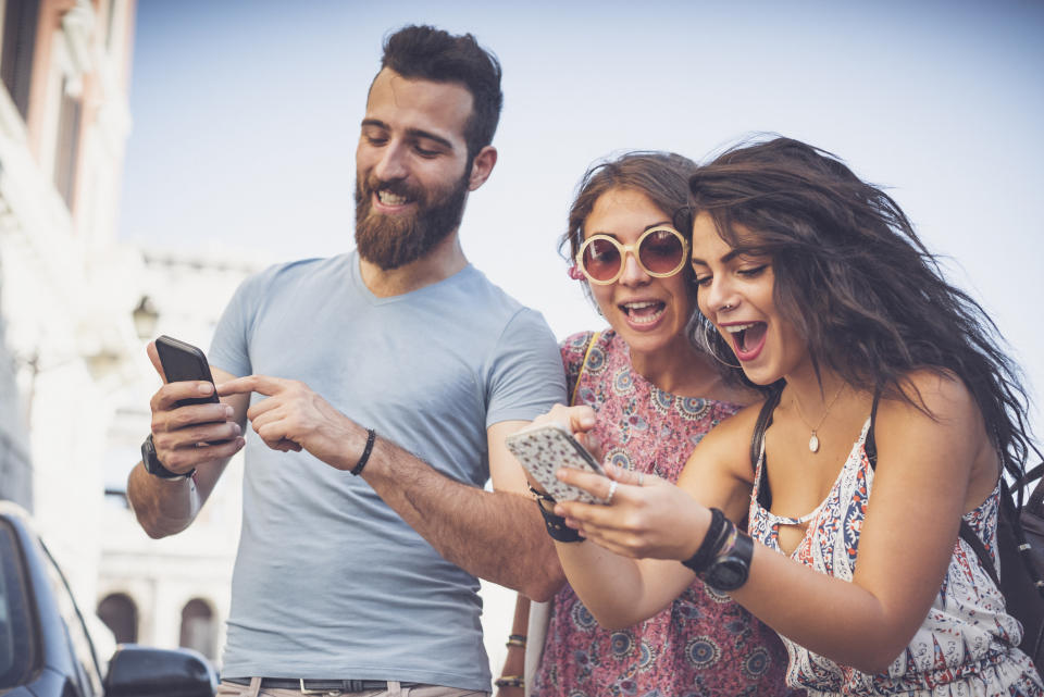 Three people excitedly looking at their phones as they stand outside