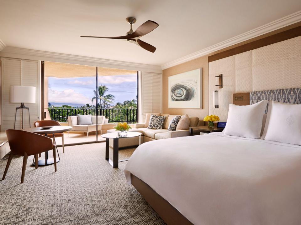 A large hotel room with a king bed, table and chairs, and a couch and balcony.