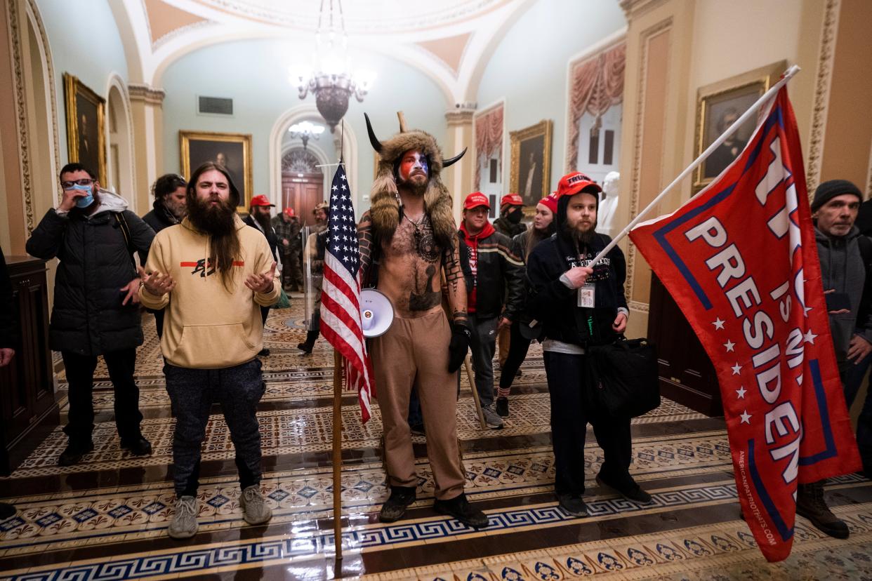 Jake Angeli, center, stands in the US Capitol dressed in fur and horns after Trump supporters stormed the building on 6 January in an effort to force legislators to overturn the election results.   (EPA)