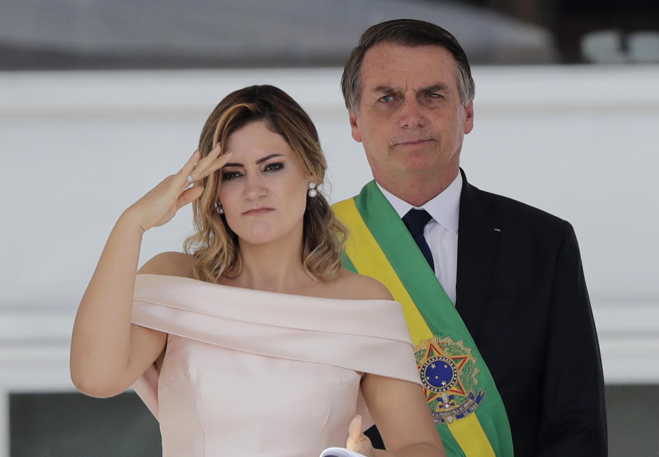 CORRECTS TO SAY SHE IS SPEAKING SIGN LANGUAGE, NOT SALUTING - Brazil's new first lady Michelle Bolsonaro uses sign language to speak to the public, as her husband, President Jair Bolsonaro, stands behind her during his inaugural ceremony at Planalto presidential palace in Brasilia, Brazil, Tuesday, Jan. 1, 2019. Another person, not in picture, translated her words for those who are not hearing impaired. (AP Photo/Silvia Izquierdo)