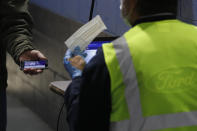 A Ford employee, left, shows his COVID-19 daily survey pass and is given a face mask as he enters the Ford Rawsonville plant, Wednesday, May 13, 2020 in Ypsilanti Township, Mich. The plant was converted into a ventilator factory, as hospitals battling the coronavirus report shortages of the life-saving devices. The company has promised to deliver 50,000 by July 4. Ford and other automakers are preparing for the reopening of their plants next week. Factories must adopt measures to protect their workers, including daily entry screening and, once they are available, the use of no-touch thermometers. Those measures already are in effect at Rawsonville. (AP Photo/Carlos Osorio)