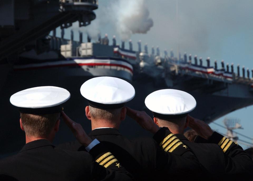 three officers salute at the decommissioning ceremony of USS John F. Kennedy