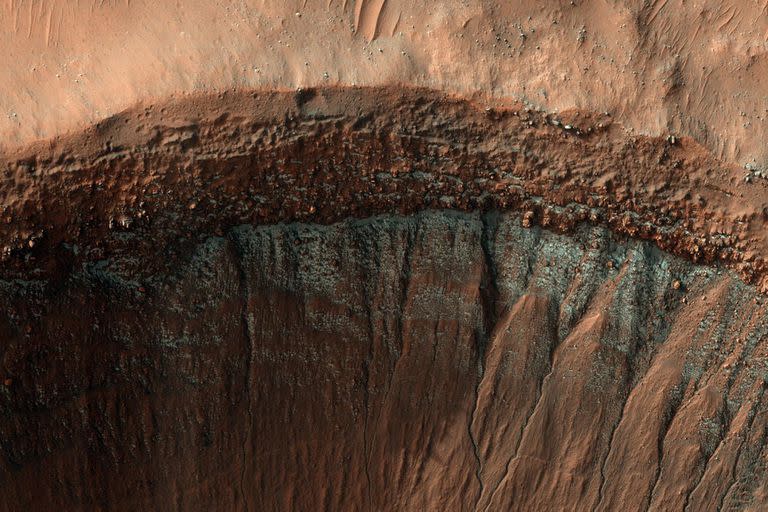 La cámara HiRISE capturó esta imagen del borde de un cráter en pleno invierno. La pendiente del cráter que mira al sur, que recibe menos luz solar, ha formado una escarcha brillante y en parches, que se ve en azul en esta imagen de color mejorado. 