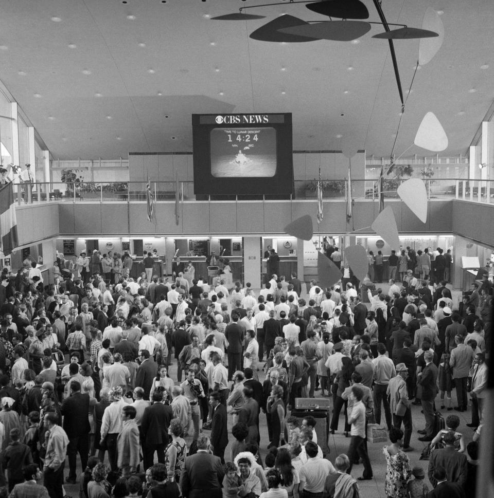 <p>the International Arrival Building at John F. Kennedy International Airport shows a crowd of passengers as they watch a large screen television that broadcasts the Apollo 11 moon landing mission, New York</p>