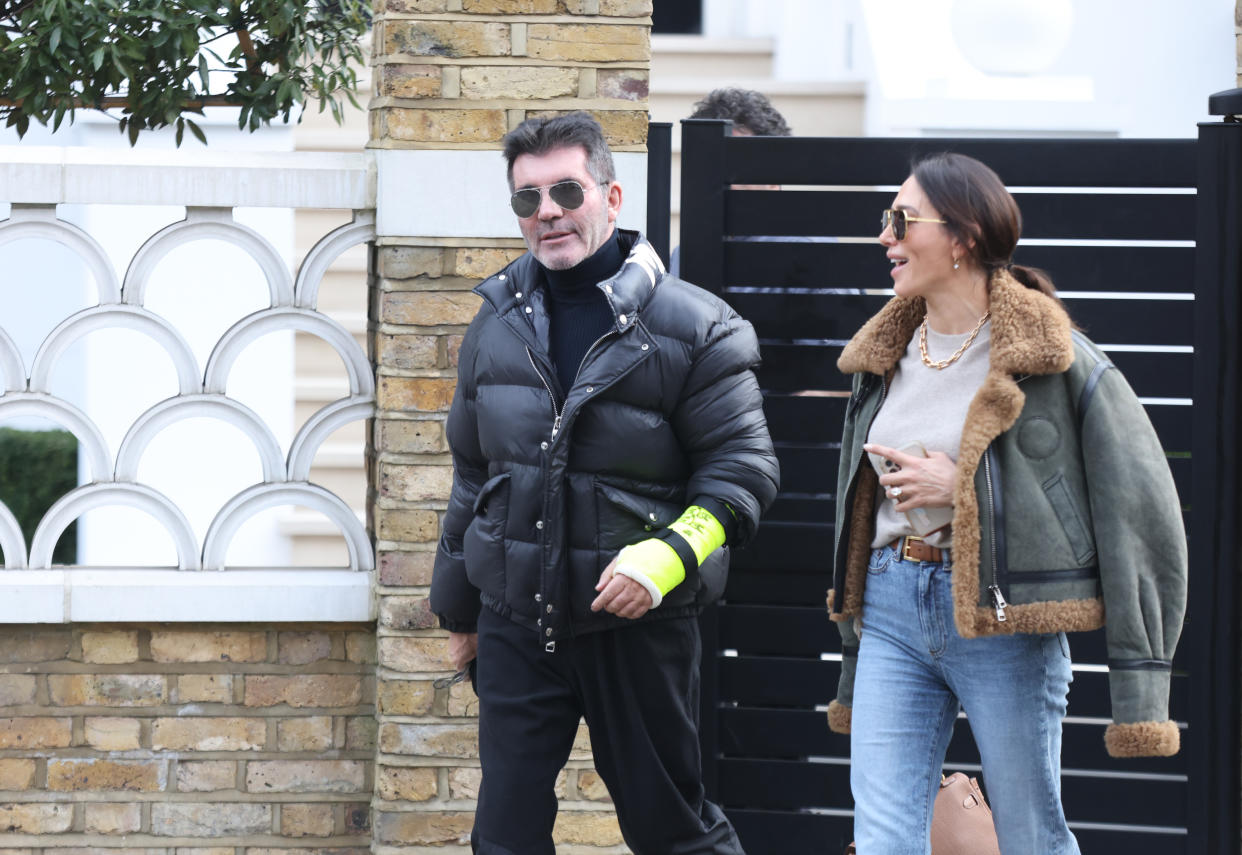Simon Cowell shows the broken arm he suffered in a bicycle injury last week as he and his partner, Lauren Silverman, leave their home in London's Holland Park. 