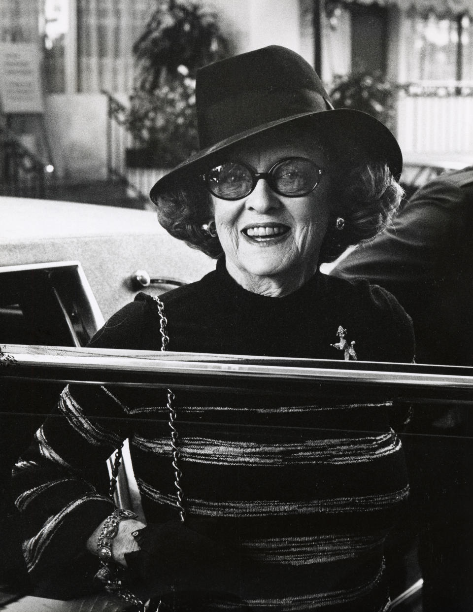 Elegant individual wearing a hat and glasses, styled in a striped outfit with a chain accessory