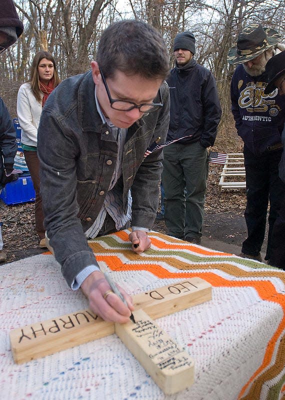 Greg Schwartz signs a cross made for Leo Murphy during a memorial service held for Murphy on Tuesday at the homeless camp in Bristol Township where he lived before dying of a heart attack in September 2010