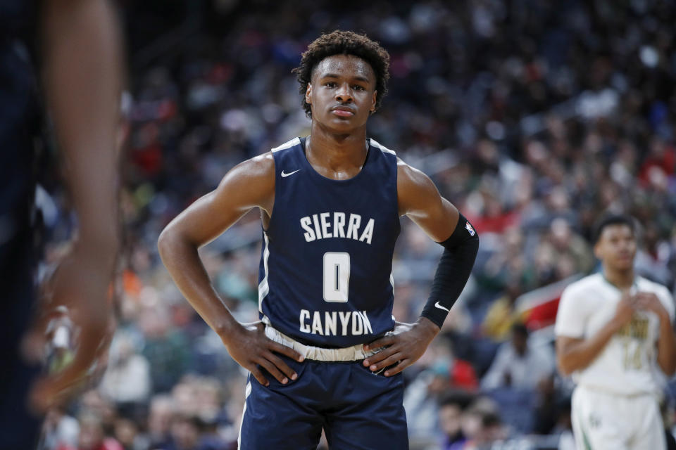 Bronny James posing with his hands on his hips, wearing a jersey on the basketball court