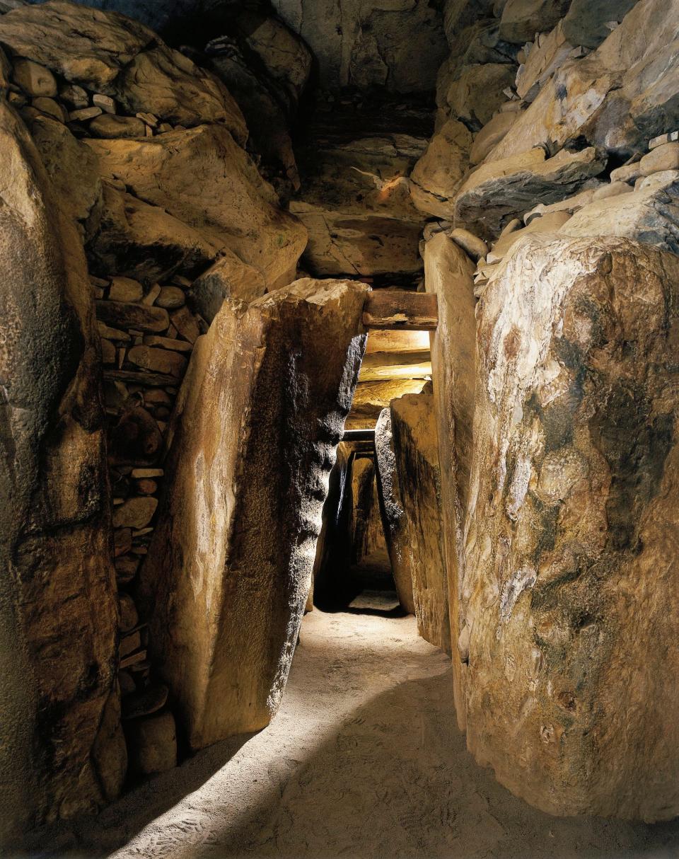 A picture shows the inside of the Newgrange monument. Narrow stone corridors are lined with drawings of animals.