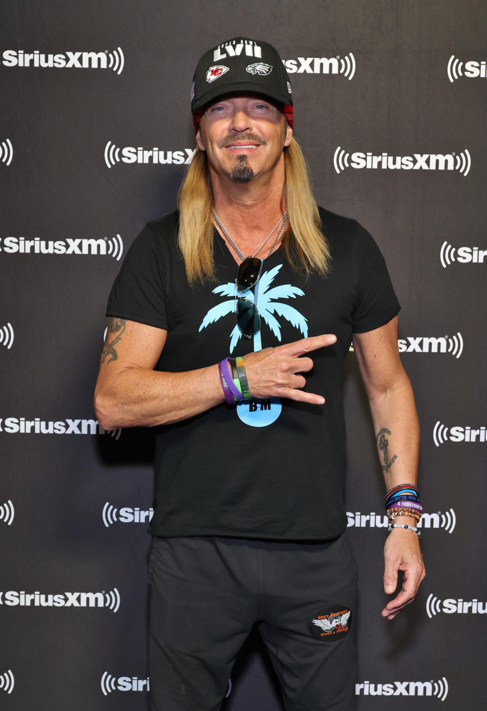 Close-up of Bret smiling and wearing a cap, shirt, and pants at a media event