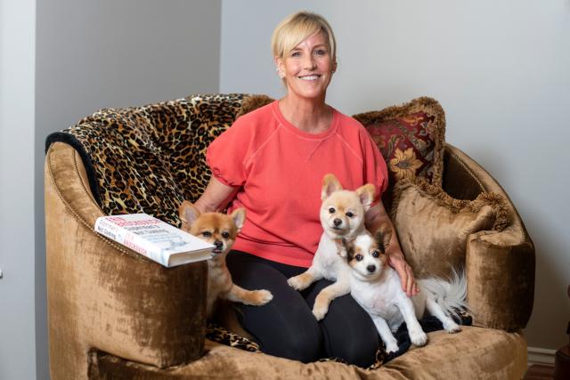 Erin Brockovich poses with three small dogs, two of whom are Pomeranians, in a large armchair.