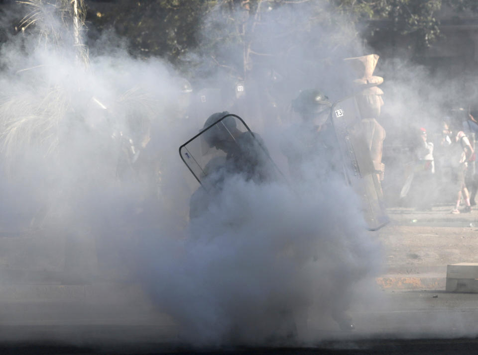 A police office is enveloped by a cloud a teargas after an anti-government demonstrator threw it back at the police in Santiago, Chile, Friday, Dec. 20, 2019. Chile marks a second full month of unprecedented social revolt that has not only altered the country's political landscape but also prompted a referendum on reforming the country's dictatorship-era. (AP Photo/Fernando Llano)