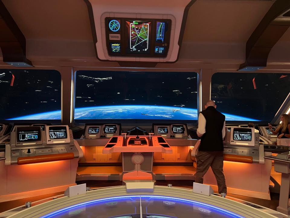 The bridge area of the Galactic Starcruiser with glowing orange control pads and screens that look like windows showing space