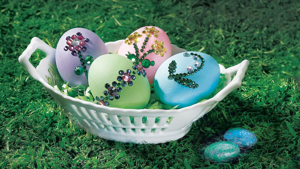 Cool Easter egg designs: Four colorful Easter eggs decorated with rhinestone flowers and displayed in a white basket on grass