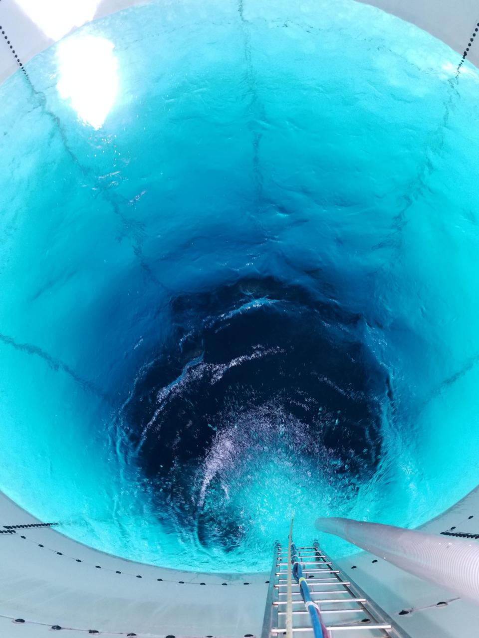 Inside of a water tower with a ladder on the side leading down to the blue water