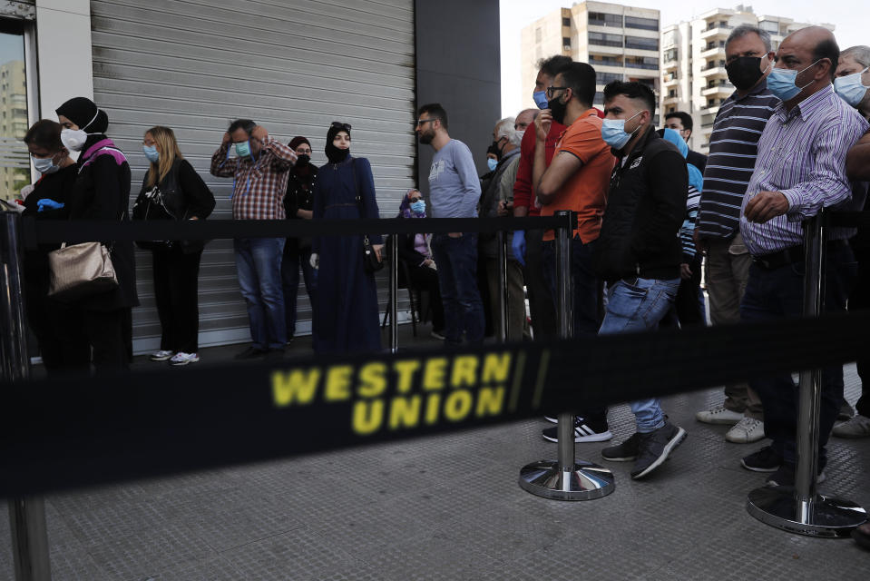 Lebanese citizens wear masks and gloves to help curb the spread of the coronavirus, as they queuing outside a Western Union shop to receive their money transfer in U.S. dollar currency, during the last day that they are allowed to dispense dollars to customers following new Central Bank rules, in Beirut, Lebanon, Thursday, April 23, 2020. Lebanon's currency continued its downward spiral before the dollar on Thursday, reaching a new low amid financial turmoil in the crisis-hit country. (AP Photo/Hussein Malla)