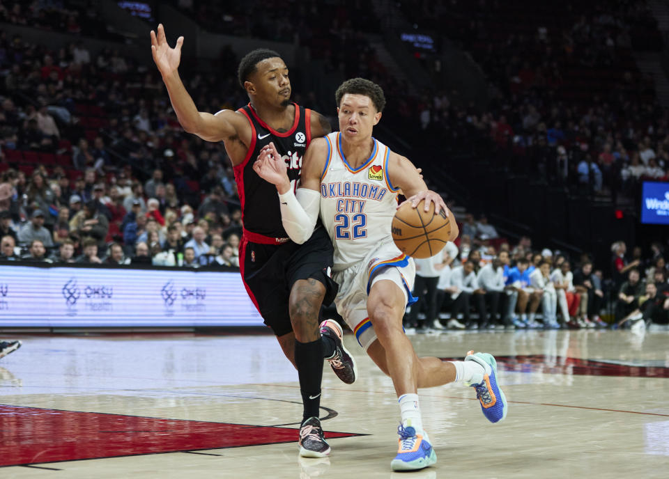 Oklahoma City Thunder forward Isaiah Roby, right, dribbles past Portland Trail Blazers forward Elijah Hughes during the second half of an NBA basketball game in Portland, Ore., Monday, March 28, 2022. (AP Photo/Craig Mitchelldyer)