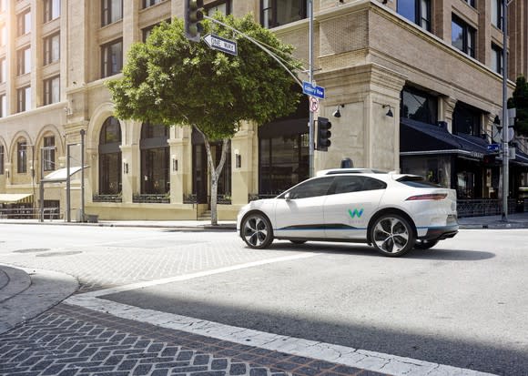 A white Waymo Jaguar iPace crossing an intersection.