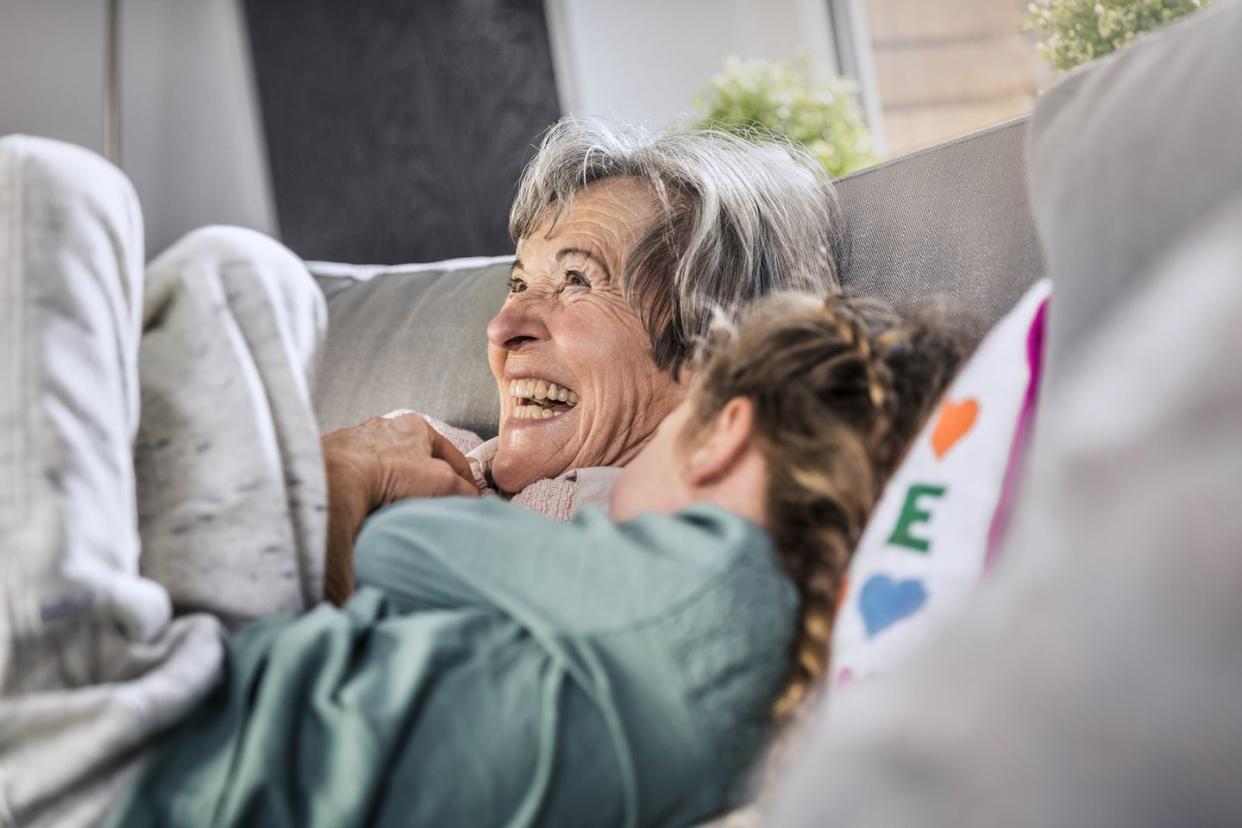 cheerful grandmother lying by granddaughter on sofa at home