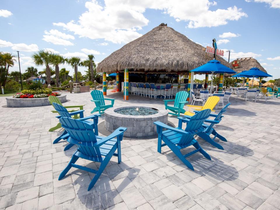 Lounge chairs surrounding a fire pit in front of a roof with a thatched pattern.