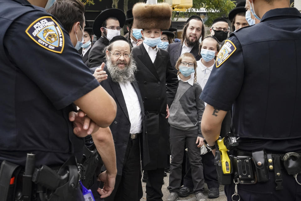 Members of the Jewish Orthodox community speak with NYPD officers on a street corner, Wednesday, Oct. 7, 2020, in the Borough Park neighborhood of the Brooklyn borough of New York. Gov. Andrew Cuomo moved to reinstate restrictions on businesses, houses of worship and schools in and near areas where coronavirus cases are spiking. Many neighborhoods that stand to be affected are home to large enclaves of Orthodox Jews. (AP Photo/John Minchillo)