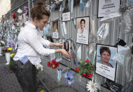 A volunteer dusts off portraits of St. Petersburg's medical workers who died from coronavirus infection during their work, hanging at an unofficial memorial in front of the local health department in St.Petersburg, Russia, Friday, Sept. 25, 2020. The number of daily new cases started to grow in late August in Russia, which has the fourth largest caseload in the world at 1.12 million infections. (AP Photo/Dmitri Lovetsky)