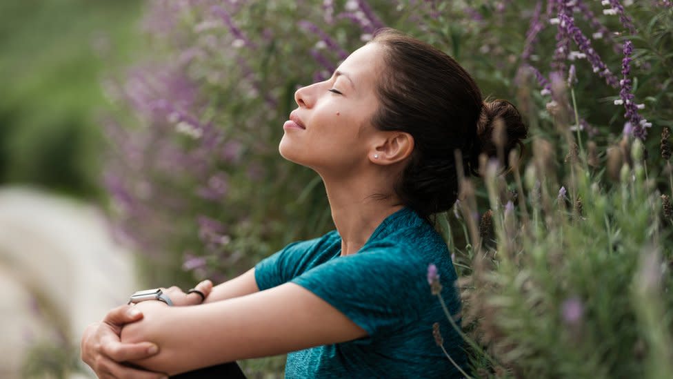 Mujer respirando junto a unas flores