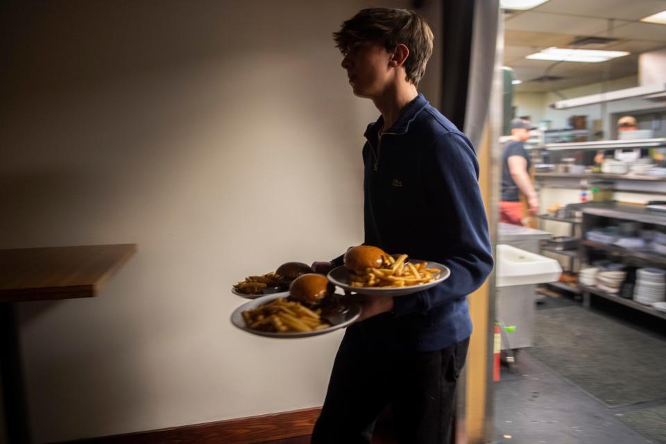 UNC Asheville student Dylan Machi, a food runner at Avenue M, carries three plates of food as he helps a server deliver orders to a table of eight at Avenue M in Asheville, February 7, 2024. Machi is included in the servers' tip share.